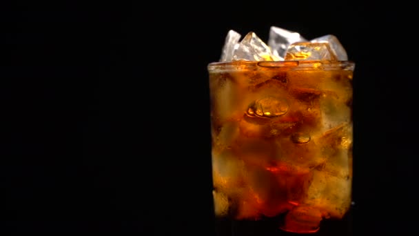 Cola met ijs en bubbels in glas draaien op zwart — Stockvideo