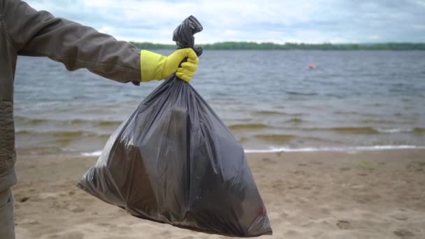 Manos voluntarias sosteniendo bolsa de basura en la playa — Vídeo de stock