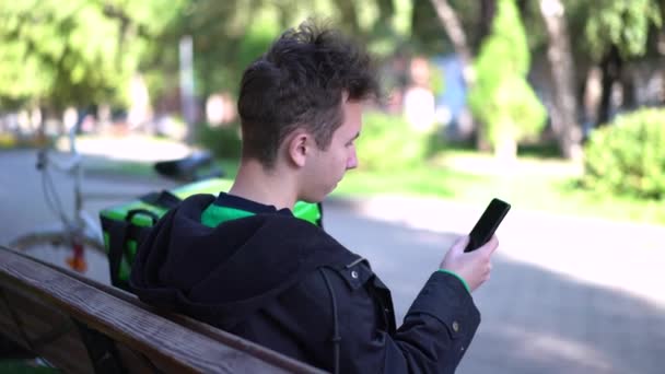 Repartidor con mochila verde y una bicicleta está buscando la dirección del cliente en el teléfono — Vídeo de stock