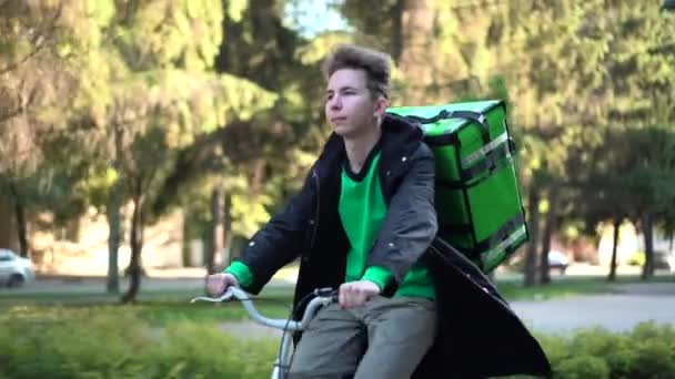 Repartidor con mochila verde pasea en bicicleta por la ciudad con comida a domicilio — Vídeo de stock