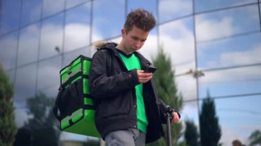 yeşil bagpack ve scooter ile teslimat adam telefonda müşteri adresi arıyor