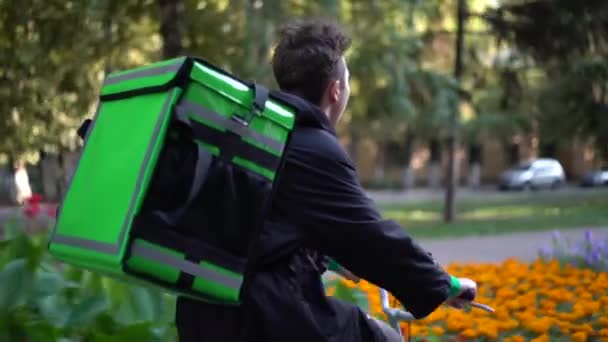 Livreur avec sac vert monte un vélo à travers la ville avec livraison de nourriture — Video