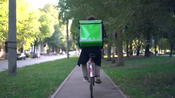 Курьер с зеленым рюкзаком едет на велосипеде по городу с доставкой еды — стоковое видео
