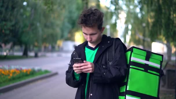 Homem de entrega com mochila verde aguardando a ordem de entrega — Vídeo de Stock