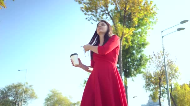 Una chica vestida de rojo paseando por la ciudad y tomando café — Vídeos de Stock