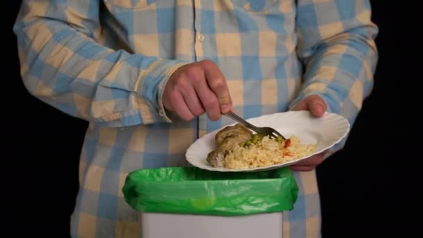 Uomo raschiando con un piatto una coscia di pollo, riso, piselli verdi nel cestino della spazzatura — Video Stock