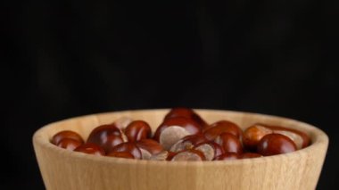 Tahta bir kasede kestaneler siyah arka planda döner.
