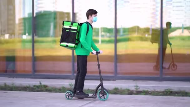 Giovane corriere che indossa una maschera medica sta effettuando una consegna dell'ordine in scooter . — Video Stock