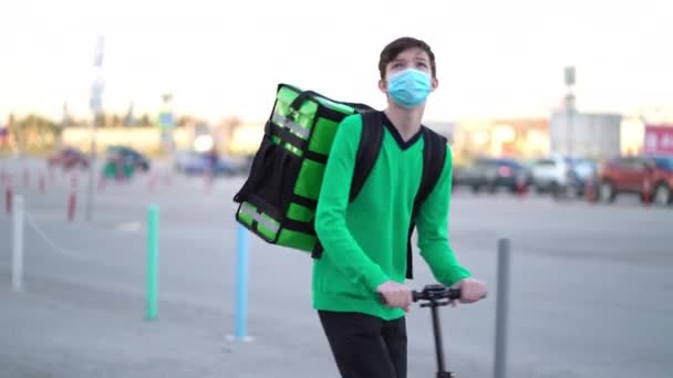 Młody kurier noszący maskę medyczną realizuje zamówienie skuterem. — Wideo stockowe