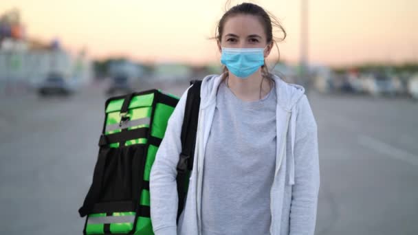 Портрет молодой женщины-курьера в медицинской маске с зеленой сумкой — стоковое видео
