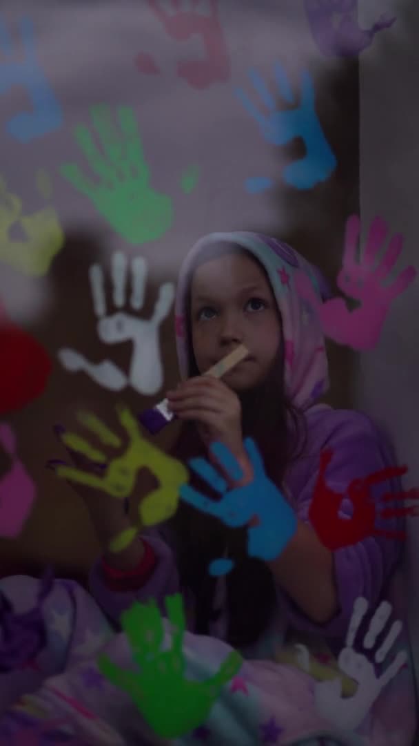 Vertikální video. školní dívka v pyžamu barva s dlaněmi na okně. — Stock video