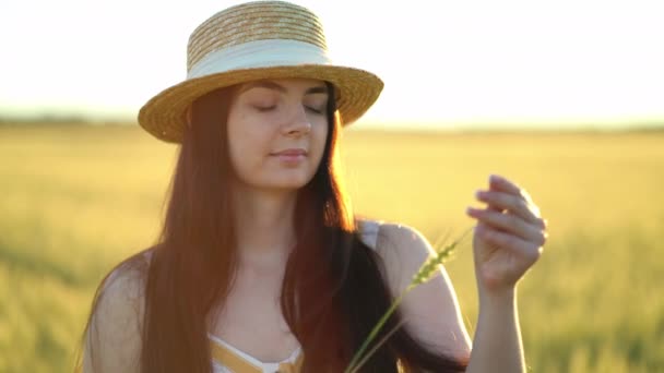 Hermosa joven con un sombrero sostiene una espiga de trigo en sus manos — Vídeo de stock