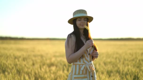 Hermosa joven con un sombrero sostiene una espiga de trigo en sus manos — Vídeo de stock
