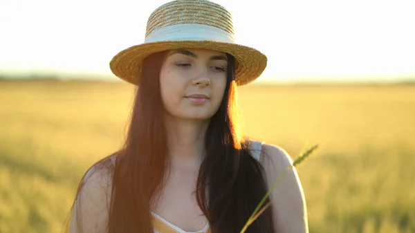 Mulher bonita com um chapéu segura uma orelha de trigo em suas mãos — Fotografia de Stock