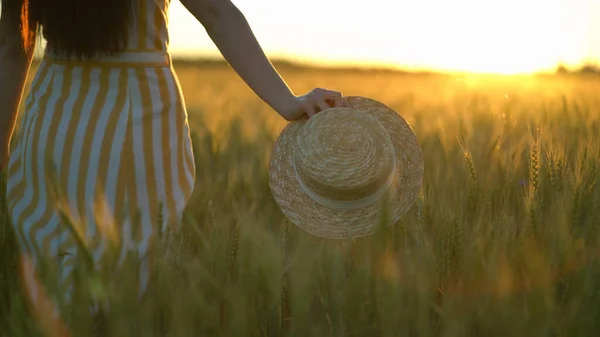 Schöne junge Frau mit Hut in der Hand geht über die grüne Wiese. Romantische Frau spaziert an Sommertagen auf dem Feld — Stockfoto