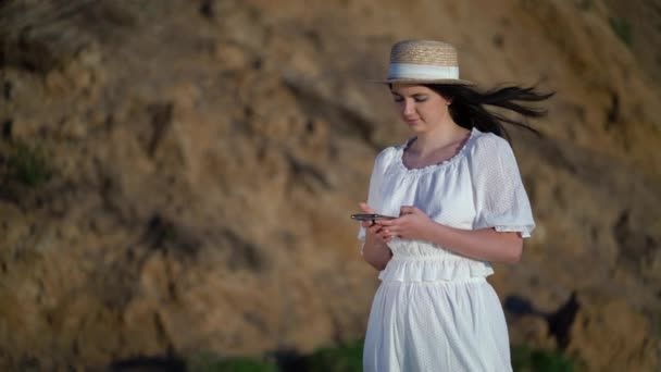 Туристка смотрит на сотовый телефон и стоит на берегу моря — стоковое видео