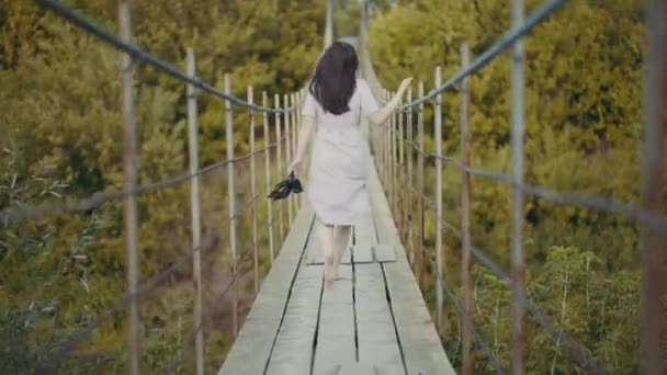 Žena v krásných šatech, běhá po mostě v lese — Stock video