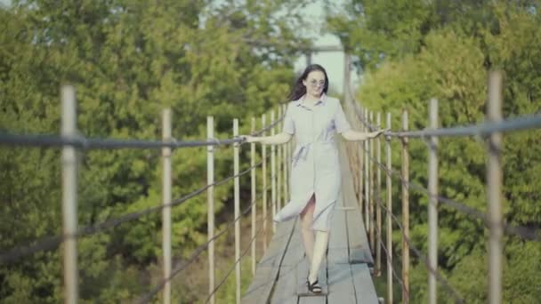 Žena v krásných šatech, kráčí po mostě v lese — Stock video