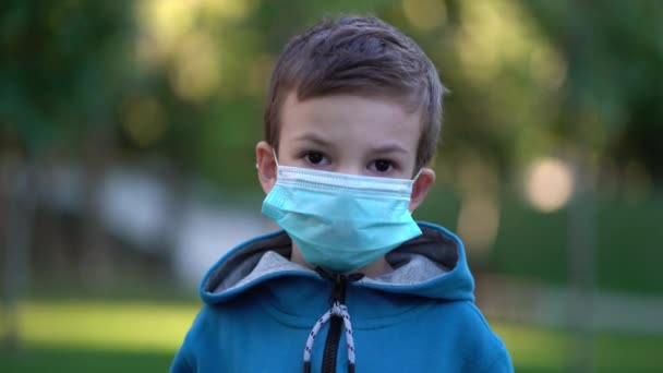 Pandemie, portrét malého chlapce s lékařskou obličejovou maskou stojící venku. — Stock video
