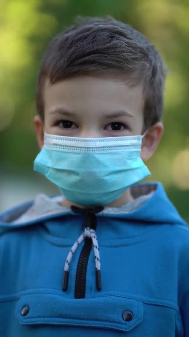 Pandemi, porträtt av liten pojke med medicinsk ansiktsmask stående utomhus. — Stockvideo