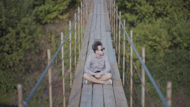 Cara caminha na ponte suspensa na floresta — Vídeo de Stock