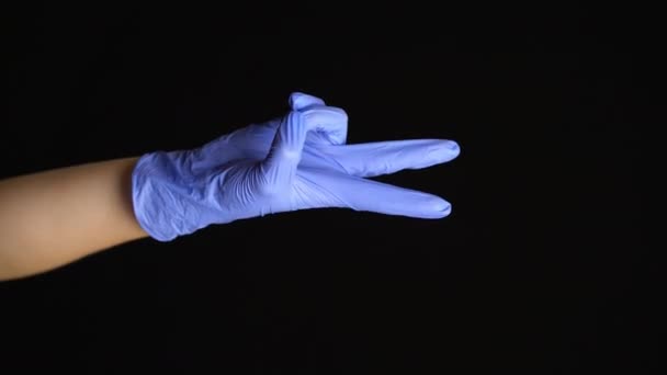 Γυναικείο χέρι σε ένα ιατρικό γάντι λατέξ κάνει μια χειρονομία ειρήνης που απομονώνεται σε μαύρο φόντο — Αρχείο Βίντεο
