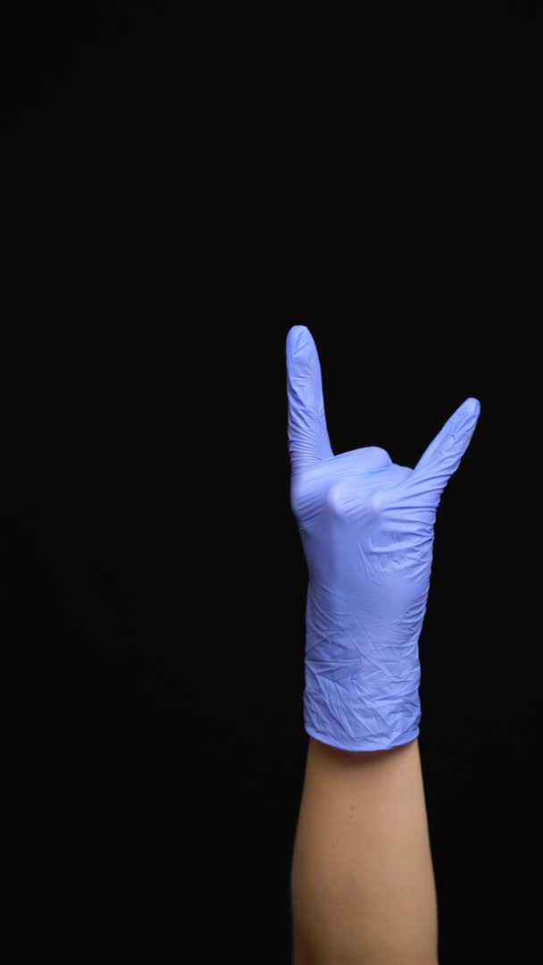 Žena ruka v latexové lékařské rukavici dělá rock gesto izolované na černém pozadí — Stock video