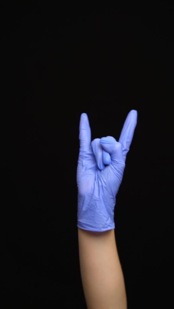 Mão feminina em uma luva médica de látex faz um gesto de rocha isolado em fundo preto — Vídeo de Stock