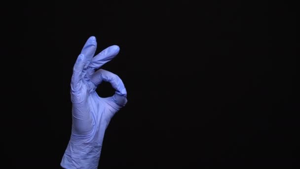 Mano femenina en un guante médico de látex hace un gesto ok aislado sobre fondo negro — Vídeo de stock