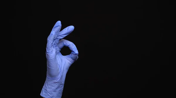 Женская рука в латексной медицинской перчатке делает нормальный жест изолирован на черном фоне — стоковое фото