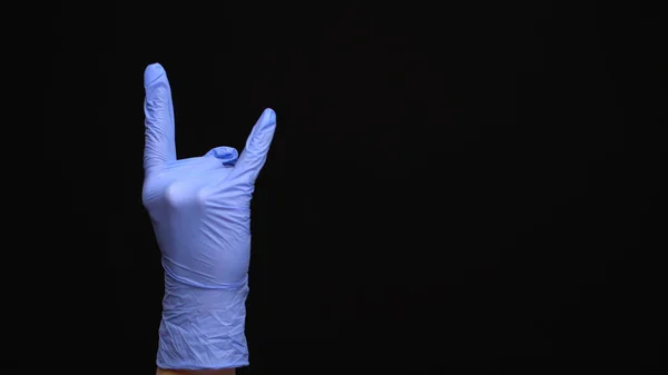 Weibliche Hand in einem medizinischen Latex-Handschuh macht eine rockige Geste isoliert auf schwarzem Hintergrund — Stockfoto