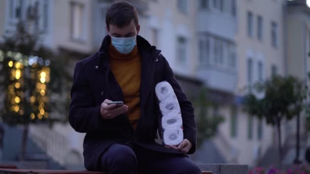 Mannen zit op bank in medisch masker met toiletpapier en smartphone tijdens de tweede golf quarantaine coronavirus COVID-19 pandemie — Stockvideo