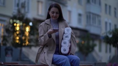 Kadın, ikinci dalga karantina Coronavirus COVID-19 salgını sırasında tuvalet kağıdı ve akıllı telefonuyla kürsüde oturuyor.