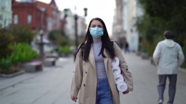 Frauen gehen in medizinischer Maske mit Toilettenpapier während der zweiten Quarantäne-Welle des Coronavirus COVID-19 Pandemie — Stockvideo