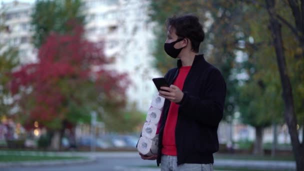 Teen walking in medical mask with toilet paper and smartphone during the second wave quarantine coronavirus COVID-19 pandemic — Stock Video