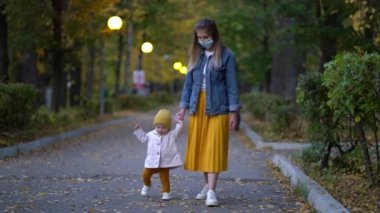 Maskeli anne, ikinci dalga karantina Coronavirus COVID-19 salgını sırasında sevgili kızının elini tutuyor.