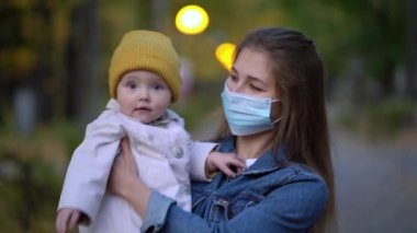 Maskeli anne, ikinci dalga karantina Coronavirus COVID-19 salgını sırasında sevgili kızının elini tutuyor.
