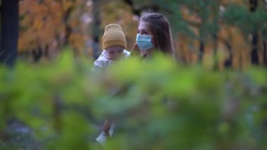 Maskeli anne, ikinci dalga karantina Coronavirus COVID-19 salgını sırasında sevgili kızının elini tutuyor.