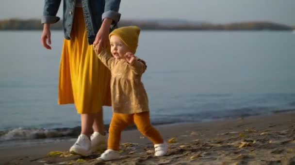 Η μαμά κρατάει την κόρη της από το χέρι και της μαθαίνει να περπατάει στην παραλία. — Αρχείο Βίντεο