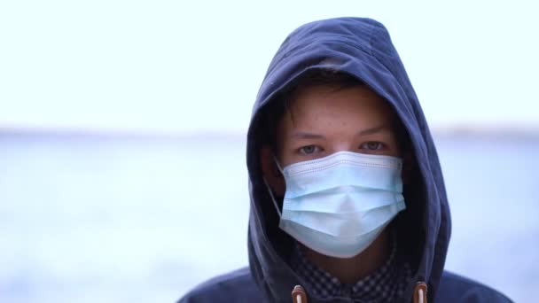 Jongen medisch masker op zijn gezicht tijdens quarantaine staat op het strand tijdens de tweede golf quarantaine coronavirus COVID-19 pandemie — Stockvideo