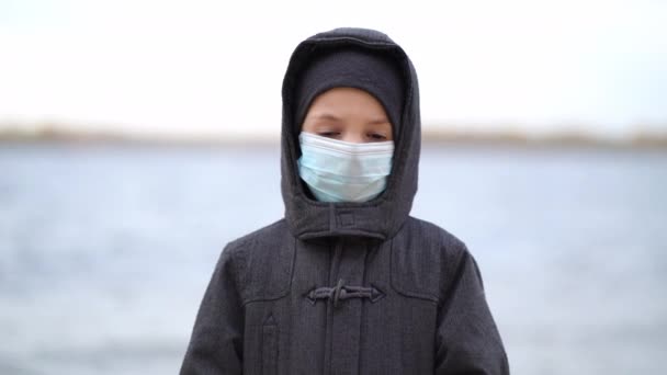 Jongen medisch masker op zijn gezicht tijdens quarantaine staat op het strand tijdens de tweede golf quarantaine coronavirus COVID-19 pandemie — Stockvideo