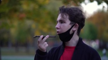 Akıllı telefon kullanırken ve sokak ortasında sesli mesaj gönderirken koruyucu maskeli bir genç.