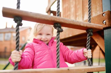 Sevimli küçük kız açık sahada eğleniyor. İlkbahar/Yaz/Sonbahar aktif spor eğlence çocuklar için. Çocuk oyun için açık havada ahşap donanımları