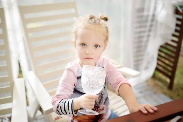 かわいい幼児の女の子は美しいガラスから水を飲みます 笑顔と魅力的な子 金髪巻き髪のお嬢さん — ストック写真