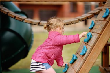 Sevimli küçük kız açık sahada eğleniyor. İlkbahar/Yaz/Sonbahar aktif spor eğlence çocuklar için. Çocuk oyun için açık havada ahşap donanımları