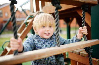 Sevimli küçük çocuk açık sahada eğleniyor. İlkbahar/Yaz/Sonbahar aktif spor eğlence çocuklar için. Çocuk oyun için açık havada ahşap donanımları