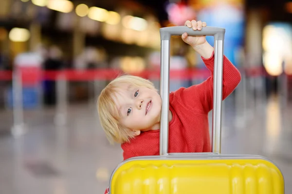 フライトの前に空港で大きな黄色いスーツケースのかわいい幸せな小さな男の子 魅力的な子供待機搭乗ターミナル 子コンセプトで家族旅行 — ストック写真