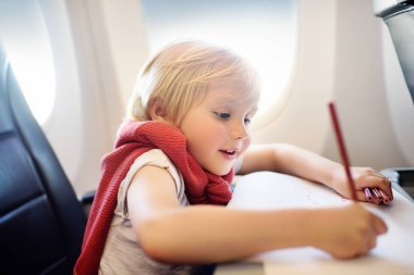 Uçakla seyahat eden sevimli bir çocuk. Neşeli küçük çocuk uçuş sırasında uçak penceresinin yanında oturuyor. Küçük çocuklarla hava yolculuğu.