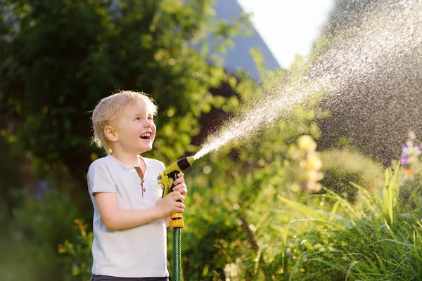 日当たりの良い家の裏庭の庭のホースで遊んで面白い少年 未就学児の子は 水のスプレーを楽しんでします 子供のための夏の屋外活動 — ストック写真