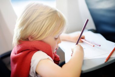 Uçakla seyahat eden sevimli bir çocuk. Neşeli küçük çocuk uçuş sırasında uçak penceresinin yanında oturuyor. Küçük çocuklarla hava yolculuğu.
